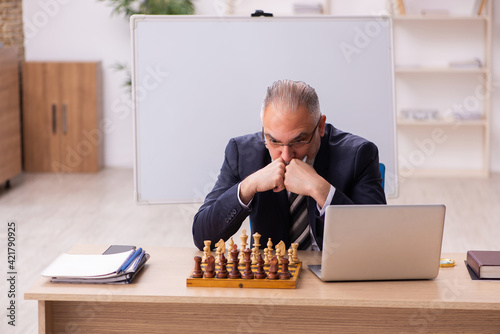 Old male employee playing chess at workplace