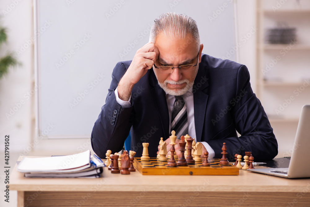 Old male employee playing chess at workplace Old male employee playing chess at workplace