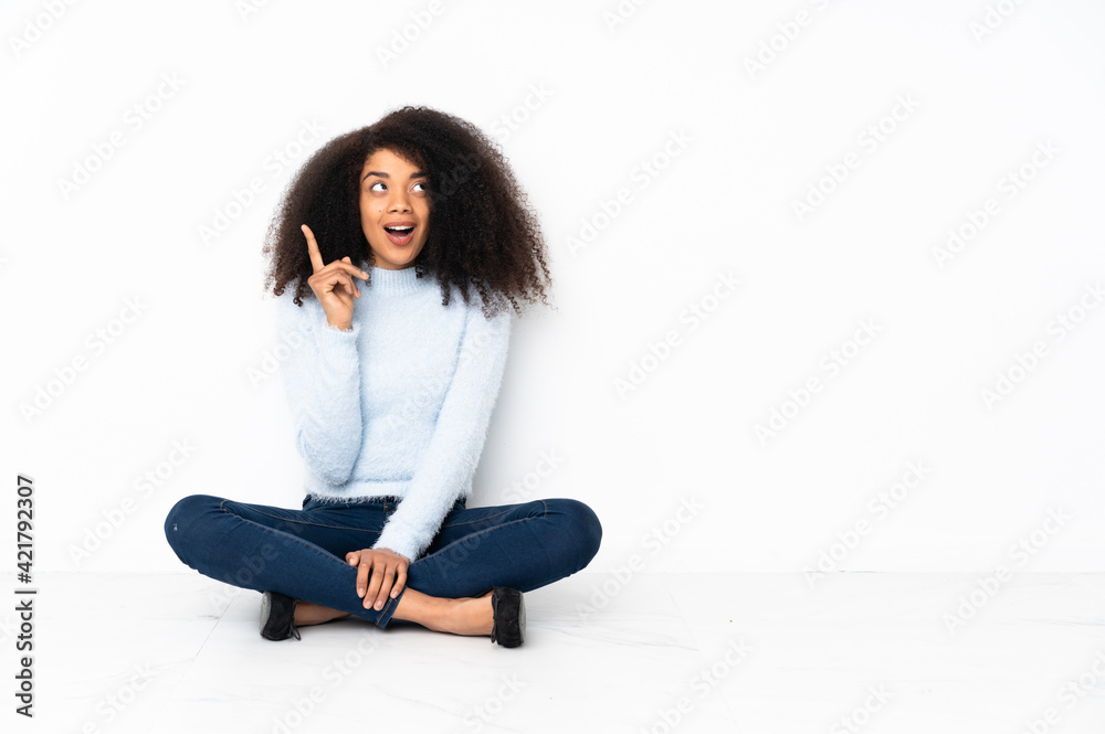Young african american woman sitting on the floor thinking an idea pointing the finger up Young african american woman sitting on the floor thinking an idea pointing the finger up