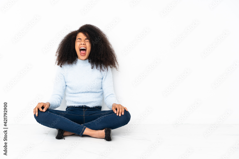 Young african american woman sitting on the floor shouting to the front with mouth wide open Young african american woman sitting on the floor shouting to the front with mouth wide open