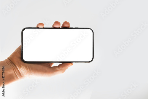 Woman hand holds smart phone with white screen. Hand showing new smartphone with blank screen. Woman holding phone from the bottom side.