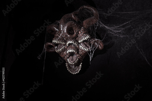 A terrible monster with teeth hangs on the wall. Black background. Sharp teeth.