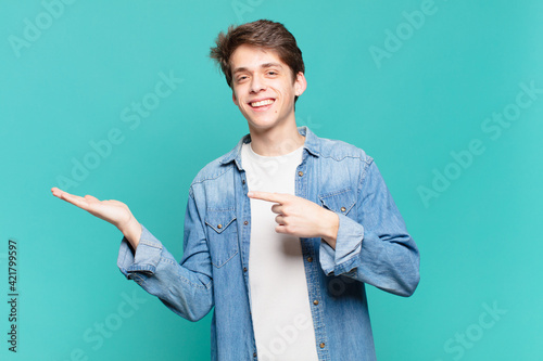 Fotografia young boy smiling cheerfully and pointing to copy space on palm on the side, sho