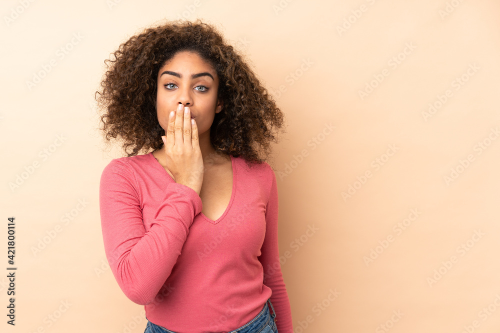 Young African American woman isolated on beige background covering mouth with hand Young African American woman isolated on beige background covering mouth with hand