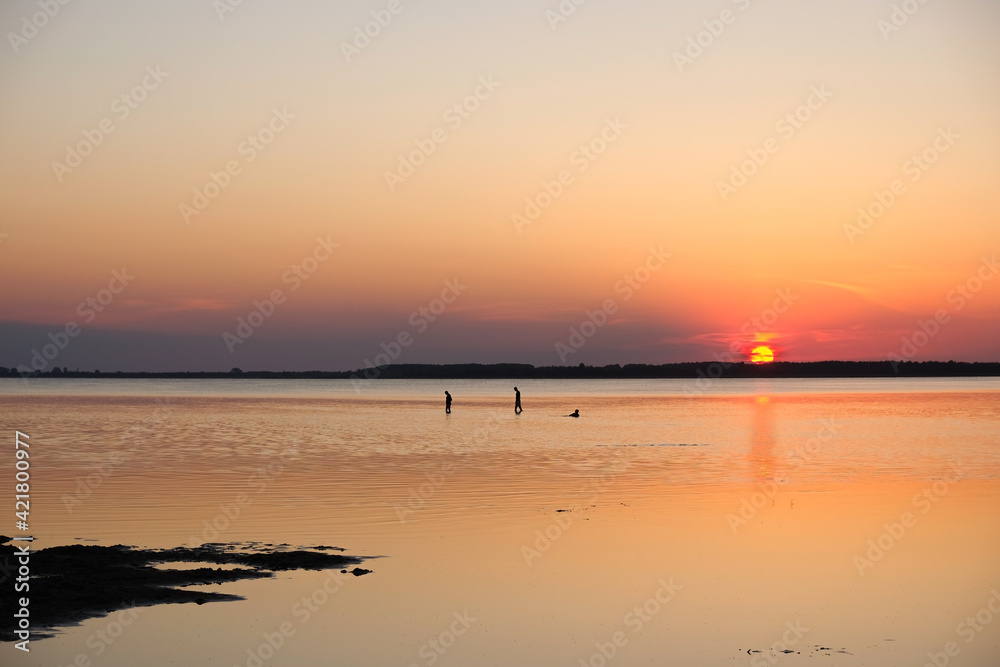 Human silhouettes on sunset background. The sunny path on the water. Lake Svityaz, Ukraine. Copy space.