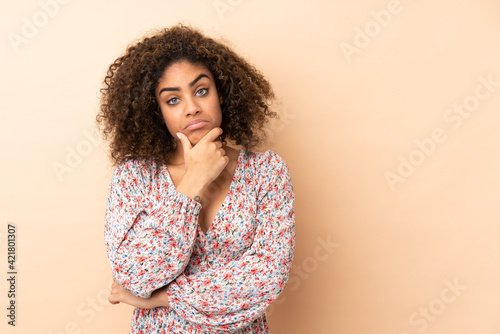 Young African American woman isolated on beige background having doubts