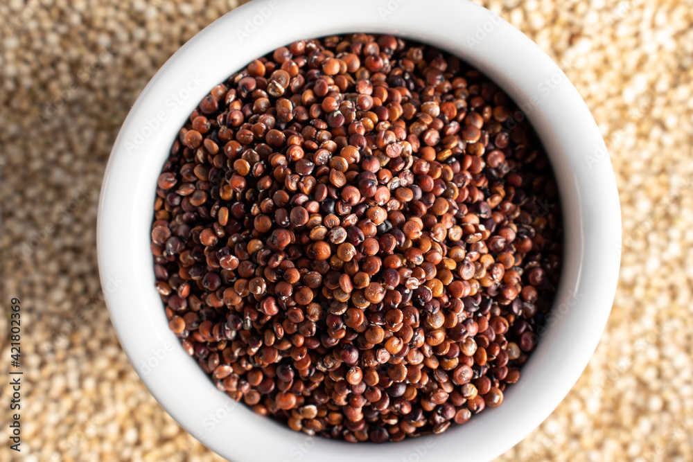 Red quinoa in white bowl on white quinoa, top view Red quinoa in white bowl on white quinoa, top view