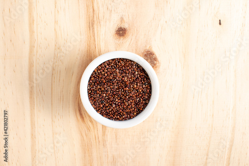Red quinoa in white bowl on wood
