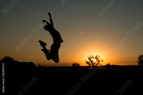 silhouette of a girl jumping up against the background of the sun setting over the horizon