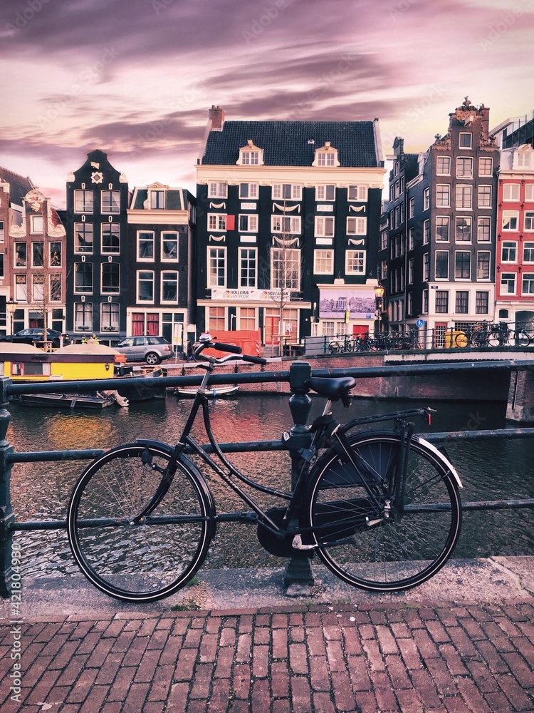 Bicycle On A Bridge In Amsterdam With Singel Canal And Houses In The Background