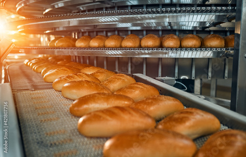 Foto Automatic line for the production of bakery products with a loaf on a conveyor belt, equipment in the workshop of a confectionery factory, industrial food production
