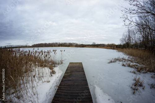 Wooden pier on a frozen winter lake. Deserted cold calm winter landscape. © Ilya