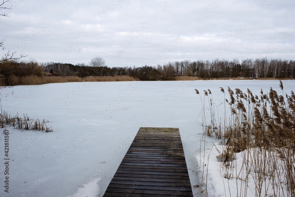 Naklejka premium Wooden boat dock on a frozen winter lake. Deserted cold calm winter landscape.