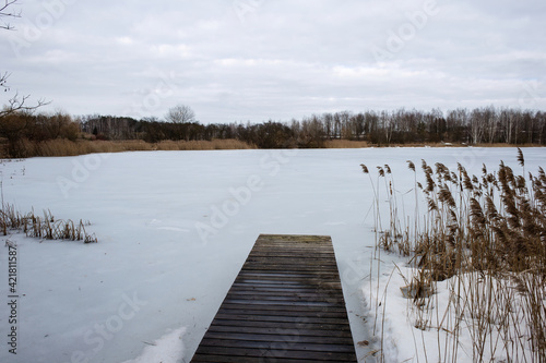 Wooden boat dock on a frozen winter lake. Deserted cold calm winter landscape. © Ilya