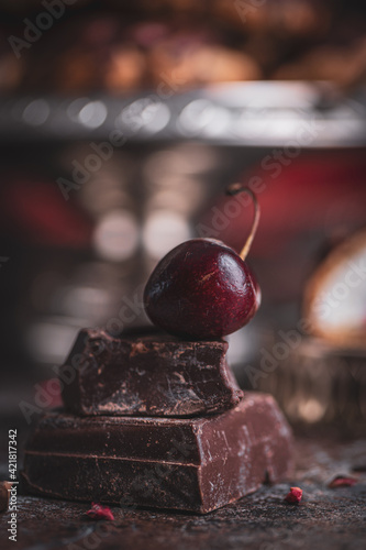 Piece of cracked dark chocolate with cherry on the top. Dark background, copy space photo