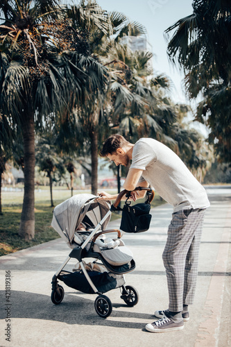 Young handsome father walking with his baby girl in the stroller around green park with palm trees