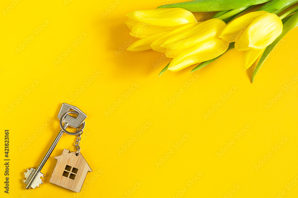 Key ring in the shape of wooden house with key on yellow background and spring tulips. Building, design, project, moving to new home, mortgage, rent and purchase real estate, summer offer. Copy space Key ring in the shape of wooden house with key on yellow background and spring tulips. Building, design, project, moving to new home, mortgage, rent and purchase real estate, summer offer. Copy space