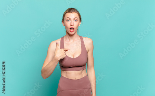 young blond woman looking happy, proud and surprised, cheerfully pointing to self, feeling confident and lofty. sport concept