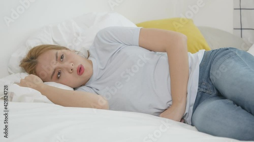 Asian woman wore are epigastric abdominal pain while lying in bed with morning sun in a white bedroom.	 photo