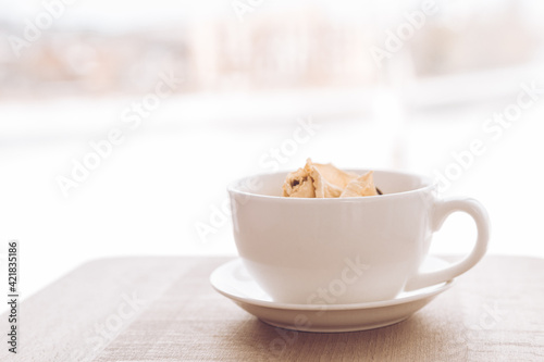 A small cup for tea with a saucer on the background of a beautiful view from the window. A cup for coffee with a flower bud inside.