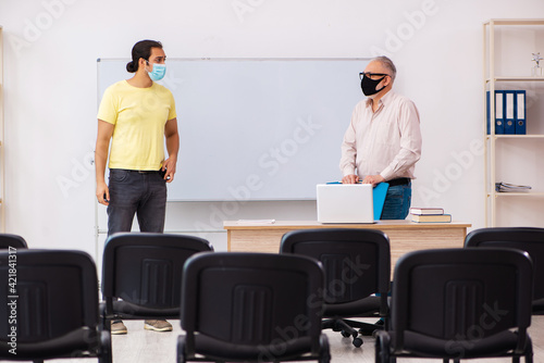 Young male student and experienced teacher in pandemic concept