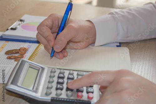 Close up man hand using calculator and writing make note with calculate about cost at home office