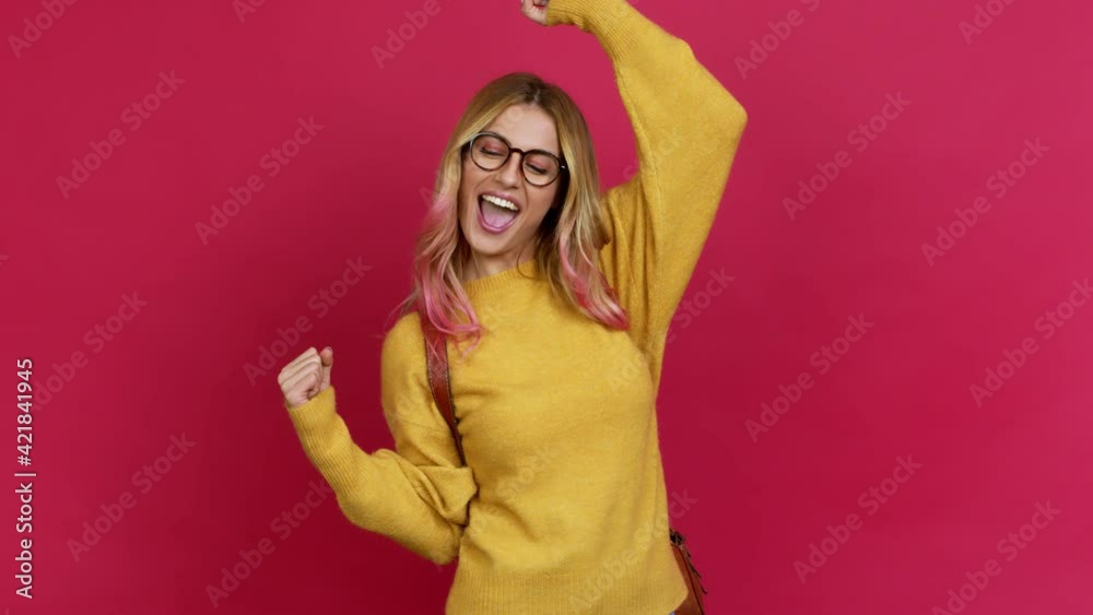 Young blonde woman with backpack celebrating a victory and surprised to be successful over isolated background