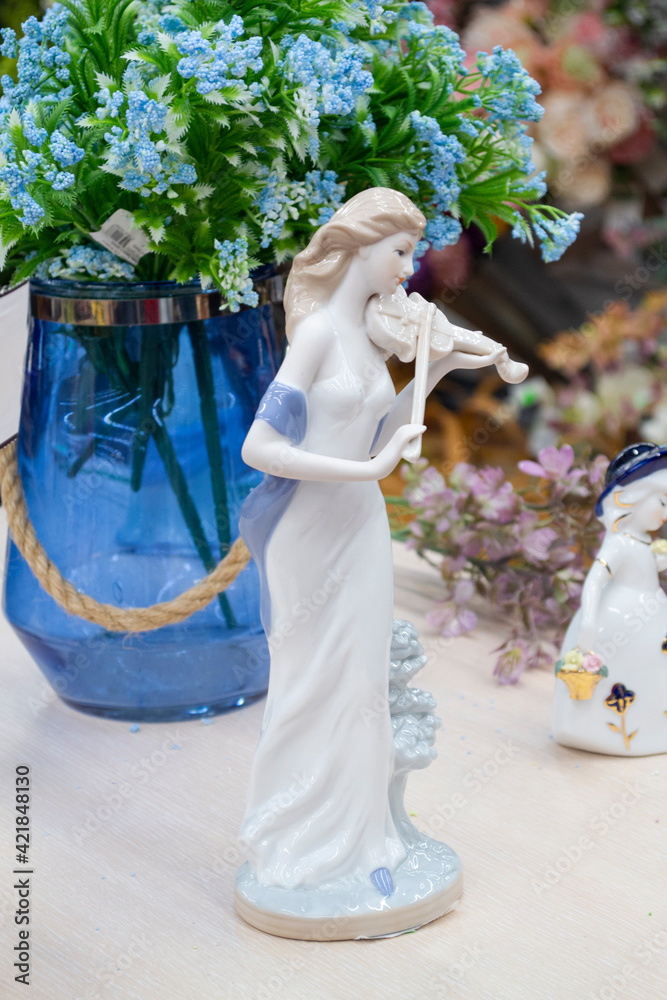 Obraz premium German porcelain figurine of a violinist girl. Ceramic figurine of the violoncellist in retro style with blue flowers on the table