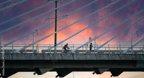 Portland, Oregon - 2-11-2021: A man on a bicycle and man running on the pedestrian path at sunset on the Tilikum cable stayed bridge over the Willamette River  in Portland Oregon photo