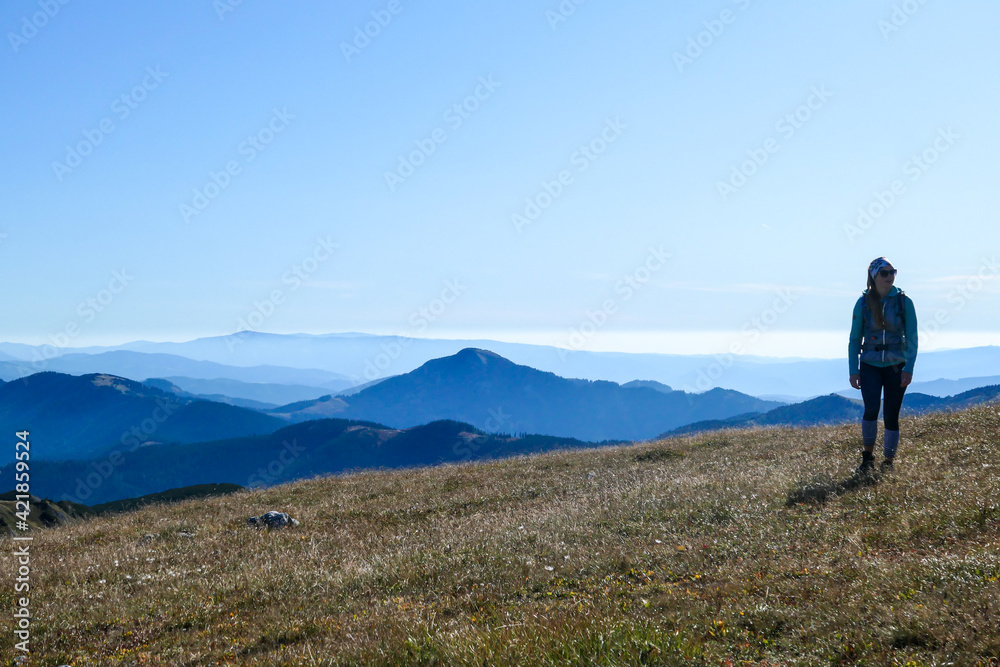 A woman with a hiking backpack hiking to the top of Hohe Weichsel in Austria. The woman in enjoying the calmness. The vast pasture is turning golden. Exploration and discovery. Endless mountain chains