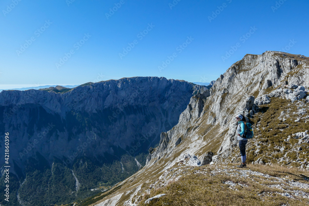 A woman with a hiking backpack standing at the edge of a high mountain, Hohe Weichsel in Austria. The woman in enjoying the view. Lush pasture around. Exploration and discovery. Endless mountain chain