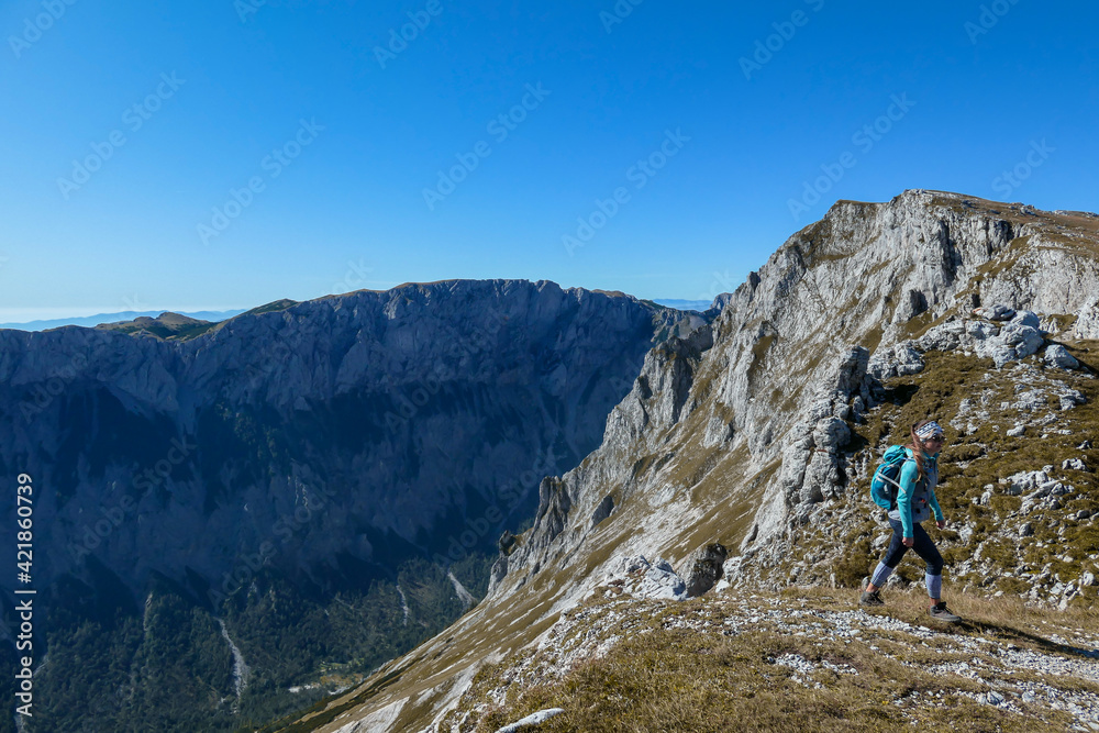 A woman with a hiking backpack standing at the edge of a high mountain, Hohe Weichsel in Austria. The woman in enjoying the view. Lush pasture around. Exploration and discovery. Endless mountain chain
