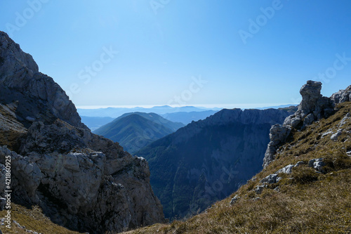 A panoramic view on Hochschwab mountain chains from the pathway leading to Hohe Weichsel. Sharp mountain slopes. Endless mountain chains, some shrouded with haze. Clear view. Blue sky above.