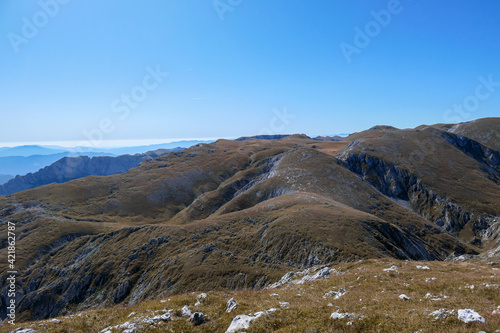 A panoramic view on Hochschwab mountain chains from the pathway leading to Hohe Weichsel. There is a vast pasture on top of a mountain, slowly turning golden. Clear view. Blue sky above. Autumn vibe © Chris