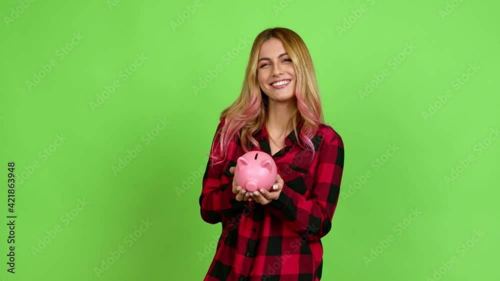 Young blonde woman unhappy and holding a piggybank over isolated background on green screen chroma key Young blonde woman unhappy and holding a piggybank over isolated background on green screen chroma key