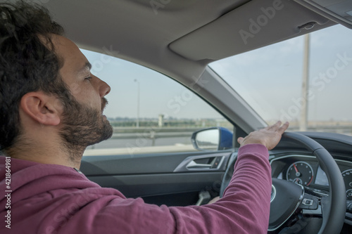 man holding steering wheel of a car and drives carefully on a highway in daylight