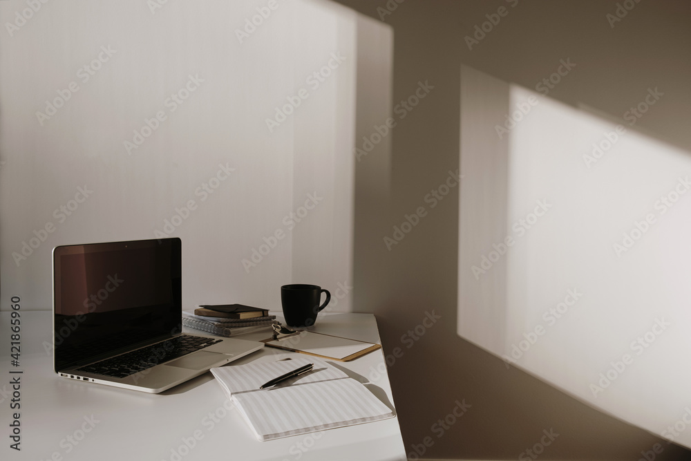 Minimalist home office desk workspace. Laptop on table with coffee cup,  paper sheet, stationery against white wall. Work, business background.  Sunlight shadow on the wall. Stock-Foto | Adobe Stock