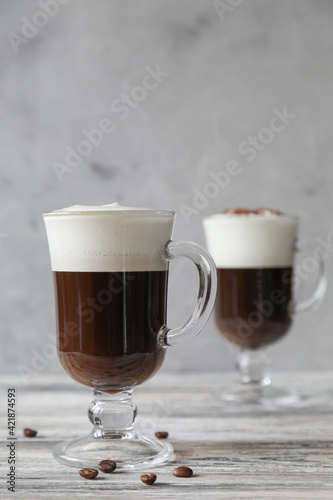 Two glass glasses with handles with Irish coffee with coffee beans on a wooden table