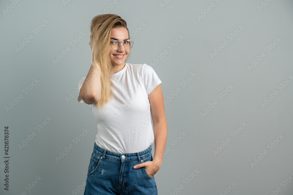 Attractive young girl wearing glasses posing beautifully on a background of gray wall. Young woman on a blank wall playfully smiling Attractive young girl wearing glasses posing beautifully on a background of gray wall. Young woman on a blank wall playfully smiling