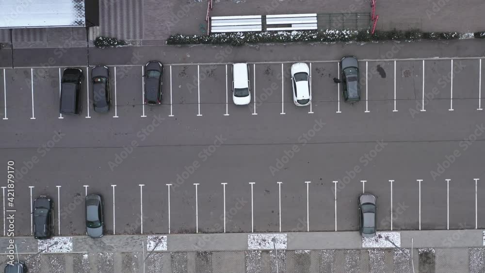 Smooth drone flight over asphalt road along parked cars in a large parking lot - Cars stand on a half-empty car parking lot - top view shooting. Smooth drone flight over asphalt road along parked cars in a large parking lot - Cars stand on a half-empty car parking lot - top view shooting.