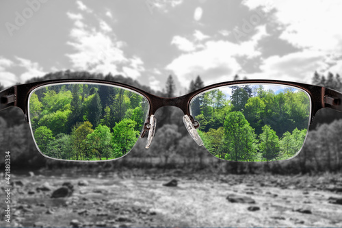 Colorful view of river and forest focused in women's glasses and monochrome background. View through eyeglasses. Better vision concept. Different world perception. photo