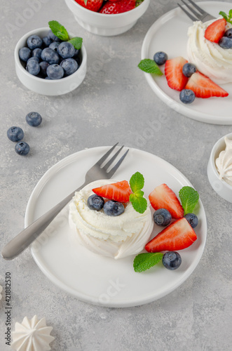 Mini Pavlova meringue cake with whipped cream and fresh berries on top on a plate on a gray concrete background. Summer dessert. Copy space.