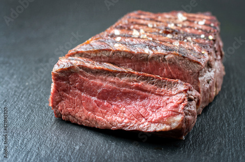 Traditional barbecue dry aged angus sirloin beef steak offered close-up on a black board
