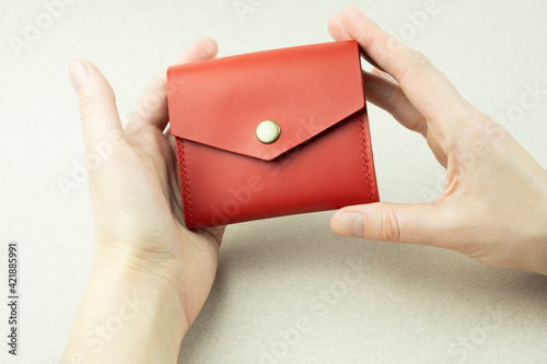 bright red leather wallet in female hands close-up on a gray background