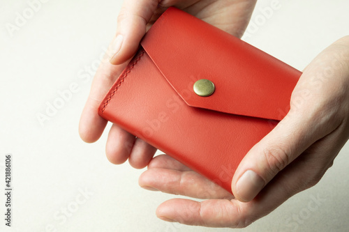 red leather wallet in female hands close-up on gray background with shadows