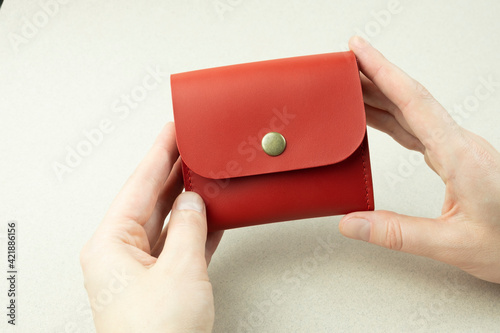 red leather wallet in hands close-up on gray background