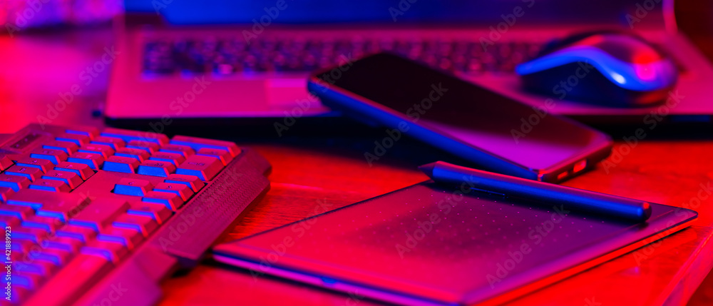 Digital designer workplace. Remote work. Freelancer workplace in neon light. Computer, laptop, graphics tablet and smartphone
