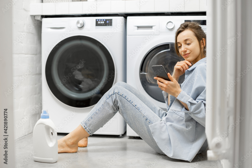 Relaxed woman with a smartphone in the laundry room Relaxed woman with a smartphone in the laundry room