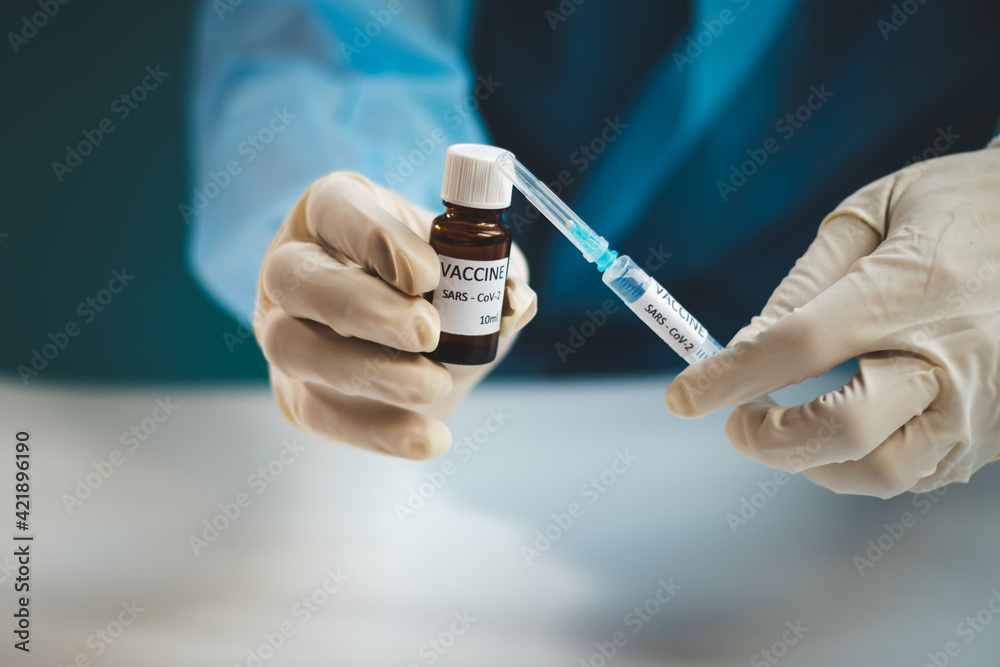 doctor in a protective shield, veil, and sterile gloved suit holds a single weapon against the Coronavirus pandemic. A scientist holds an ampoule against a Covid-19 and a syringe needle doctor in a protective shield, veil, and sterile gloved suit holds a single weapon against the Coronavirus pandemic. A scientist holds an ampoule against a Covid-19 and a syringe needle