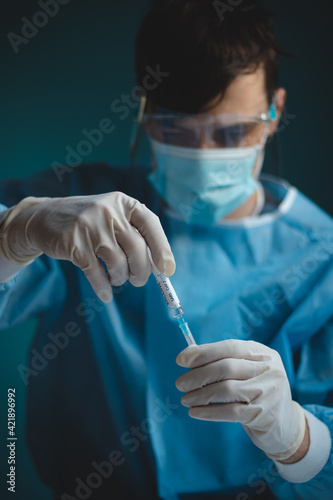 doctor in a sterile protective suit with a shield on his head prepares a syringe with a Covid-19 vaccine for an incoming patient. Medical worker. Fighting a pandemic